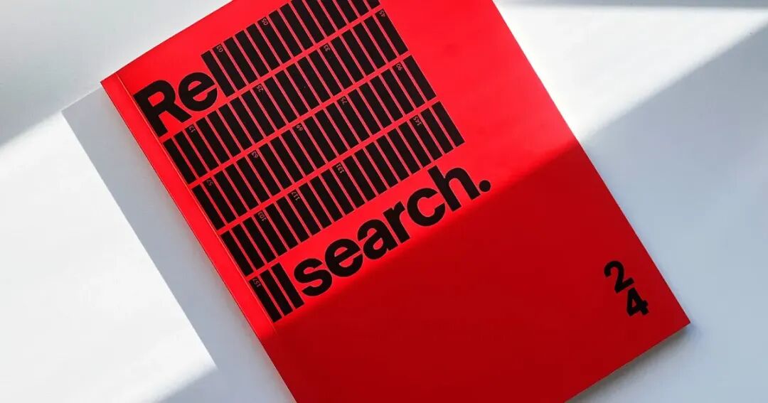 Open red publication "ReSearch" volume 24 displayed on a white surface with a distinctive shadow casting over the pages.